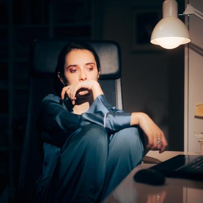 A young woman working at night looking worried staring at her laptop.