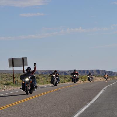 Motorbike riders raising hands for a photo opportunity while passing a road in California, USA.