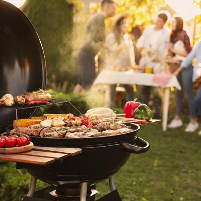 A focus on a barbecue grill set outdoors, with a group of friends having a party in the backdrop.