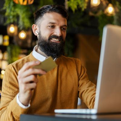 A man in a cafe happily holding a credit card while doing an online transaction.