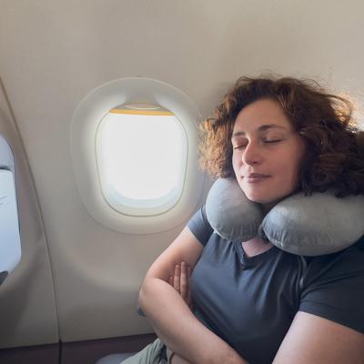A person sleeping with a neck pillow from her seat in a plane.