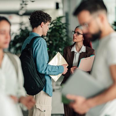 A college student talks to a professor in a campus hallway.