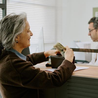 A senior woman handing money to a bank teller.