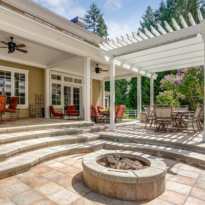 A modern luxury outdoor patio with a white pergola, fire pit, and outdoor sitting area.