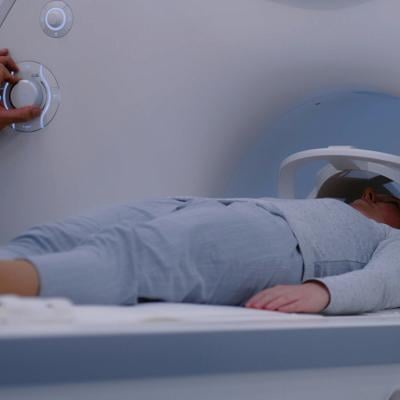 A female patient lies down on an MRI or CT scan bed moving inside the machine for scanning the brain and body. 