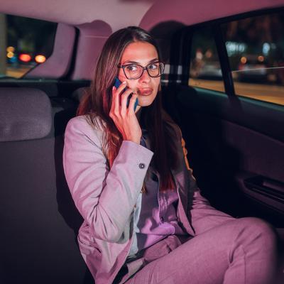 A young businesswoman in the backseat of a car late at night and talking on the phone.