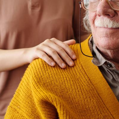 A young adult patting the shoulder of an elderly person as care and support.