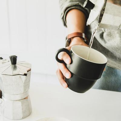 A person pouring hot water from a moka put to a cup before brewing coffee beans.