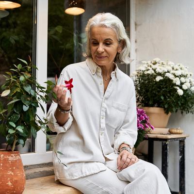 A senior woman sitting in her garden and looking at flowers.