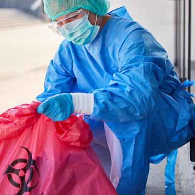 A cleaning staff in full safety gear carefully disposes biohazard waste in a clinic.