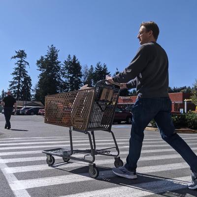 Street view of a man leaving with a supermarket with a grocery cart.