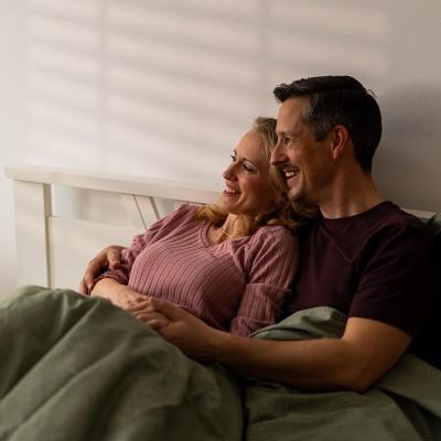 A couple sitting in bed wrapped in blankets.