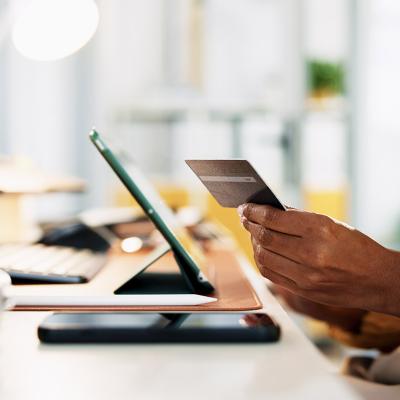 A business manager holding a credit card while checking digital transactions from a tablet. 