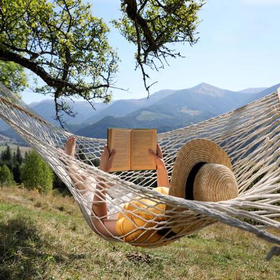 A person reading a book while relaxing in a hammock outdoors.