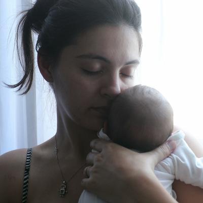 A mother holding her newborn baby by the window.