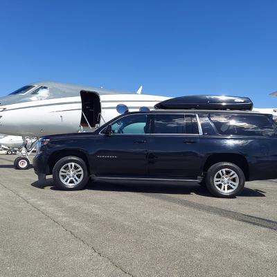 A black Chevrolet Suburban car parked alongside a private air jet in an open ground.