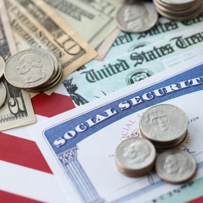 US dollar banknotes and coins, a social security form, and calculator on top of a US flag.