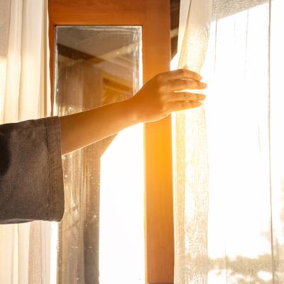 A woman's hand opening the curtains to a window to let in sunlight.