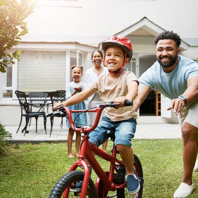 A young boy learning how to ride a bicycle being cheered on by his family.