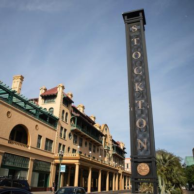 View of a street in downtown Stockton with a tall metallic sign with the city name vertically displayed in 2026.