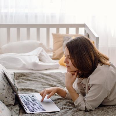 A parent working remotely from a bedroom while her baby toddler is sleeping in a crib.