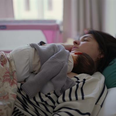 A young mother and her newborn baby napping together at home.