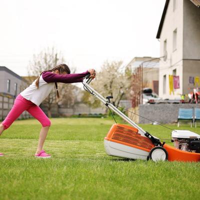 A teenager pushing an electric lawnmower in their backyard during a summer holiday.
