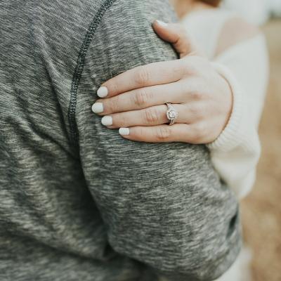 A diamond engagement ring on a woman's hand resting on her fiancé's arm.