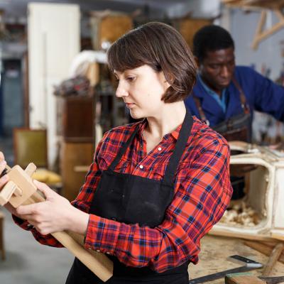 An artisan checking a wood component during a creation process of its furniture in a workshop.