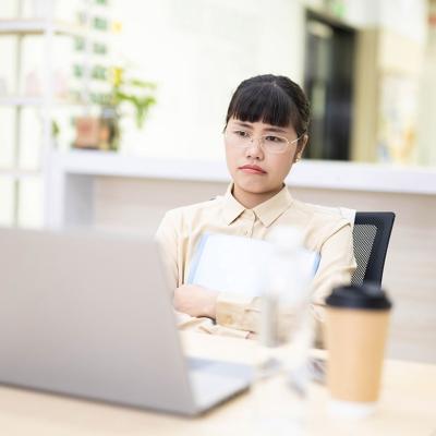 An employee thinking on a work-related matter while looking at a laptop from her office desk.