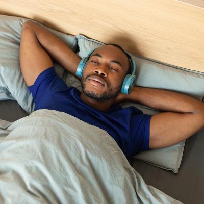 Man lying in bed with his hands on his head and wearing headphones.