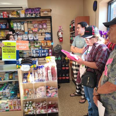 A store worker showing a "No warrant, No entry" / "Private area" signs behind the counter.