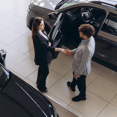 A car sales agent and a customer shaking hands after closing a deal in a car dealership shop.