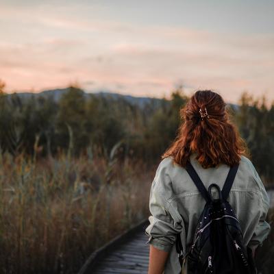A girl seen from behind with a backpack walking through nature at sunset.