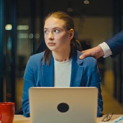A young business assistant appearing to be uncomfortable as a male colleague places a hand on her shoulder.