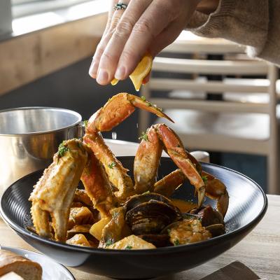 Person squeezing a slice of lemon over a crab dish.