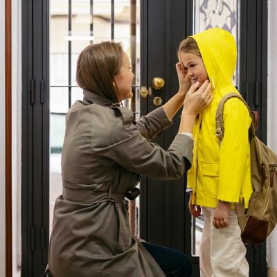 A mother preparing her child to go to school with a raincoat.