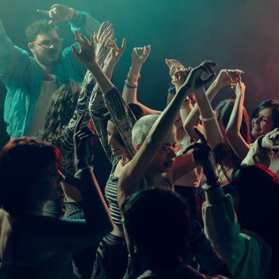 A crowd raising their hands as they dance under the lights in a club.