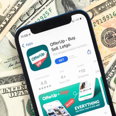 An OfferUP shopping app logo displayed from a mobile phone screen with U.S. dollar bills in the background.
