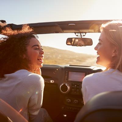 Two female friends happily riding on a highway in their convertible car.