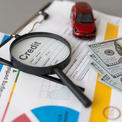 A credit loan application form with a magnifying glass, cash, and a small figure of a car on top of it.