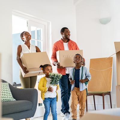A happy family of four moving into their new home, surrounded by cardboard boxes labeled for different rooms.