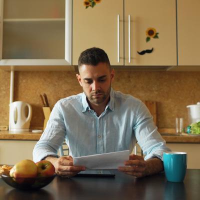 A male homeowner reading an unpaid bill letter in his kitchen.