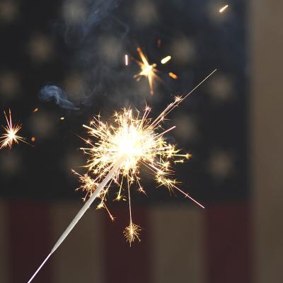 A sparkler firework with the US flag in the background for the 4th of July celebrations.