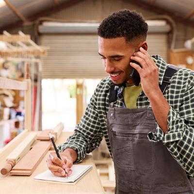 A carpenter taking a customer's order inquiry over a phone call in a furniture work shop.