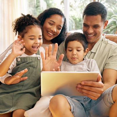 A family greeting and smiling to their relatives through a video call from a tablet at their home.