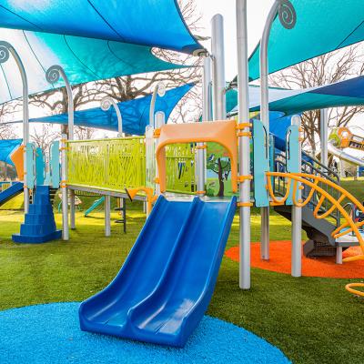 A colorful, modern playground with slides, bridge, climbing stairs, and a canopy.