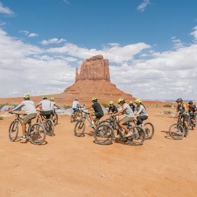 A cycling group in the Arizona desert, specifically within Monument Valley.