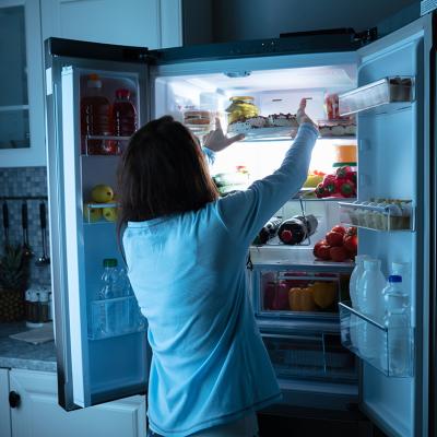 Woman storing food in the refrigerator at night.