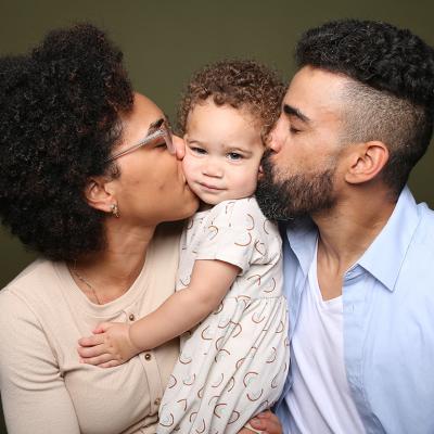 A mother and a father kissing their baby's face.